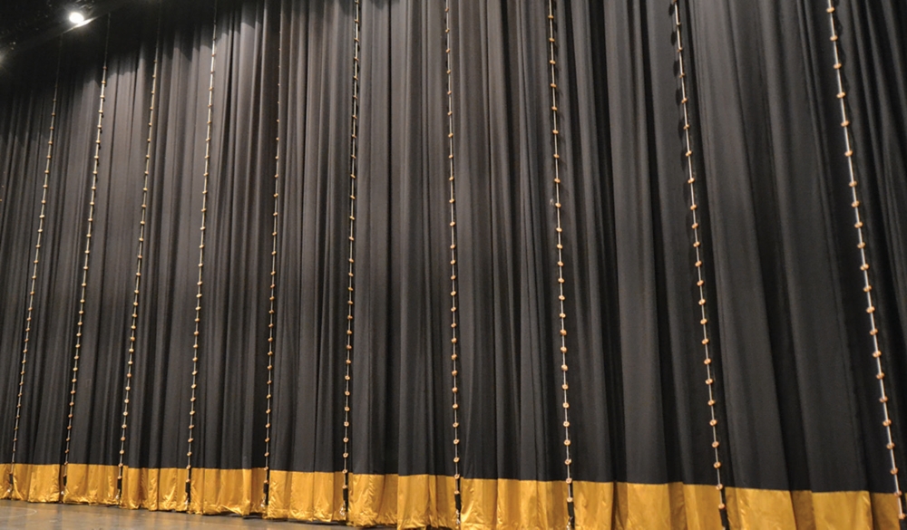 A black curtain with a gold hem and vertical tie lines